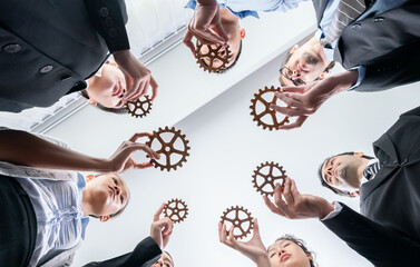 Below view group of multiracial business people joining gear wheels together as effective unity and...