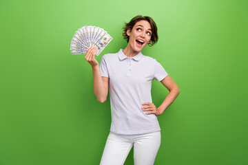 Photo of impressed funky lady wear grey t-shirt rising cash fan looking empty space isolated green...
