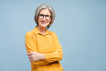 Smiling senior woman, wearing eyeglasses and blouse, looking at camera, posing arms crossed