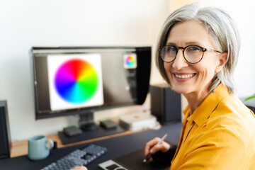 Portrait smiling senior woman, graphic designer, editor, retoucher sitting at workplace