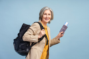 Happy positive gray haired senior woman backpacker holding passport and tickets