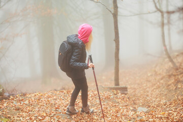 A woman equipped with a backpack and ski poles navigates through a foggy forest, surrounded by...