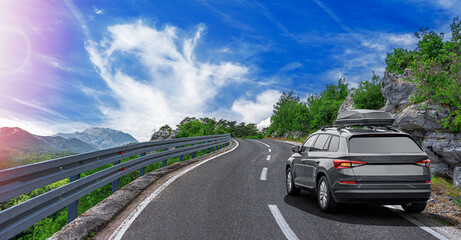 Travel car drives along the highway against the backdrop of rocky mountains on a summer day.