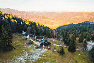 Fototapeta premium A stunning aerial view of a house nestled among the majestic mountains, surrounded by lush greenery and towering peaks under a clear blue sky