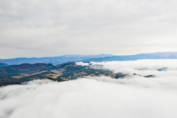 From a birds eye perspective, a magnificent mountain range emerges above a sea of fluffy white clouds, creating a surreal and breathtaking view