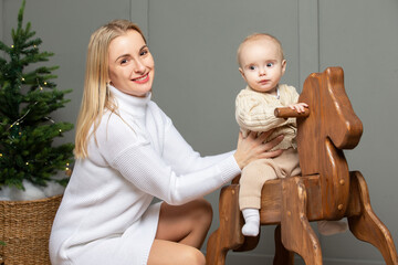 Mom rides her baby on a wooden gurney and horse in the Christmas room.