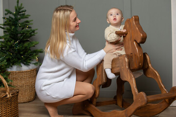 Mom rides her baby on a wooden gurney and horse in the Christmas room.