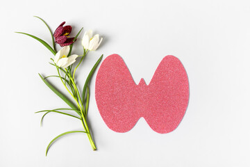 World Thyroid Day. Concept of thyroid disease and health. Pink Paper form of the thyroid gland on gray background with spring white and burgundy flowers hazel grouse