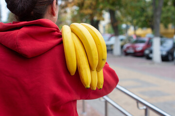 A woman holds a branch of bananas behind her back.