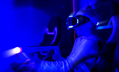 A young boy is playing a video game with a controller in his hand. The room is dimly lit, and the boy is wearing a virtual reality headset. The atmosphere of the image is one of excitement