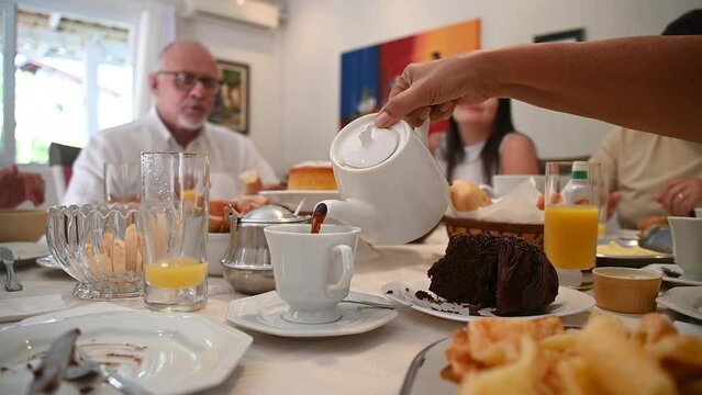  Fam&iacute;lia em casa sentada a mesa pra tomar caf&eacute; da manh&atilde;, reuni&atilde;o de fam&iacute;lia, fam&iacute;lia feliz comendo. Mesa de caf&eacute; da manha com frutas e p&atilde;o