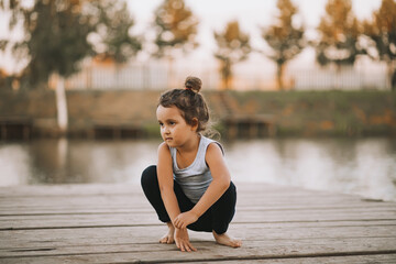 Little girl sitting in nature near by river lake and practicing yoga or resting after sports exercises. Healthy lifestyle.