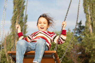 Smiling girl playing on a swing outdoor. Children summer activity.