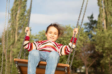 Smiling girl playing on a swing outdoor. Children summer activity.