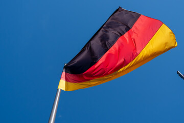 Waving German flag against a blue sky. German flag on the roof of a building.