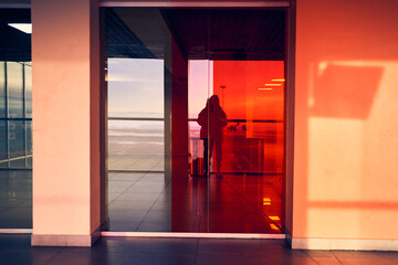 A female traveler looks at her reflection in the glass window of the airport, a tourist girl in the...