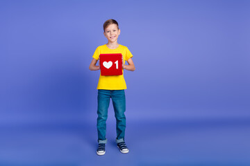 Photo of funny cheerful funny boy wear stylish yellow clothes hands hold red card poster heart symbol isolated on violet color background