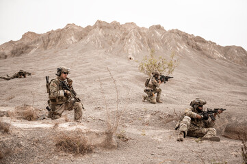 Obraz premium Soldiers in camouflage uniforms aiming with their rifles.ready to fire during military operation in the desert , soldiers training in a military operation