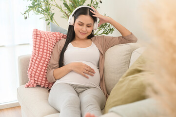 Happy pregnant woman with headphones listening to mozart music and lying on sofa, pregnancy concept - obrazy, fototapety, plakaty