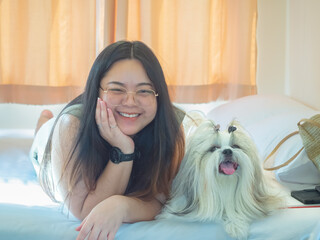 Young woman and Shih Tzu dog are comfortable together and cuddling on bed in bedroom