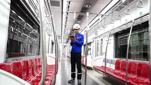 engineer inspector at a train station wears a blue uniform and a helmet, holds a walkie-talkie, and inspects safety repairs inside electric train cars at the train maintenance station.