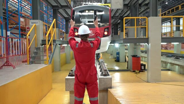 Two engineer inspector at a train station wears uniform and a helmet giving hand signals for the train to stop at the train maintenance station.