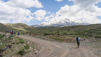 Fototapeta premium Hikers walking to the basecamp with snowy mountain summit in backdrop, Mount Ararat in Turkey