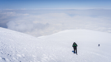 Mountaineers walking towards the snowy mountain summit above the clouds, Mount Ararat in Turkey