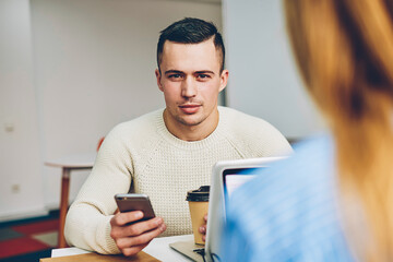 Portrait of serious candidate for vacancy looking at camera checking mail with online letter sitting in office during interview,male worker looking at camera chatting via smartphone on coffee break