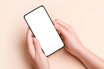 Female hand holding a phone with a blank screen on a beige background