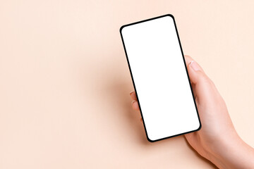 Female hand holding a phone with a blank screen on a beige background