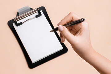 White paper on a black plate and a woman's hand about to write on a beige background