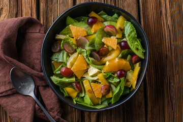 Vegetable salad with pomegranate seeds on a bright metal background, top view. Lettuce, corn salad, cucumber, avocado, orange, pomegranate.