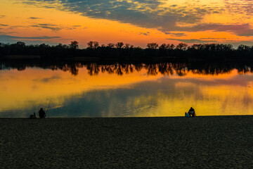 Fishermen at the bank of the river at sunset. Silhouette photo