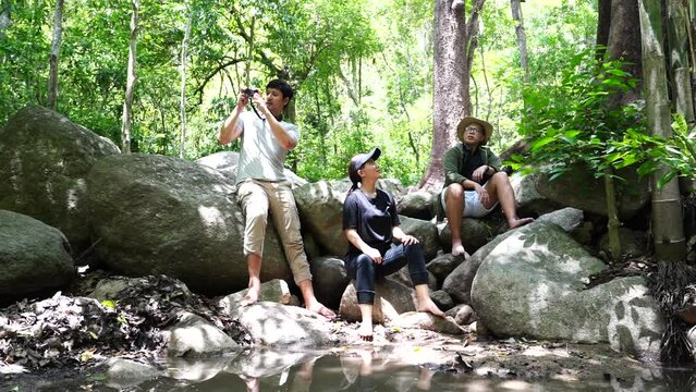 Group of three Asian friends, two men and one woman, have a good relationship, hiken rock climbing at the waterfall stream in the forest is happy summer time trip during the vacation.Lifestyle concept