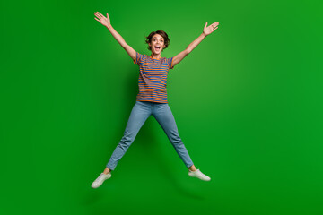 Full size portrait of astonished cheerful girl jump raise arms empty space ad isolated on green color background