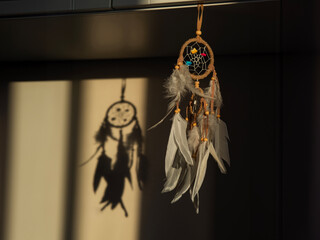 A dreamcatcher with white feathers is hanging in a dark room. The sunlight is falling on the wall...