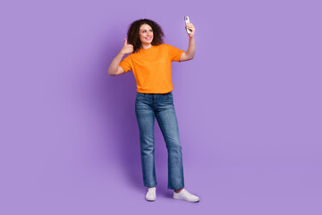 Full length photo of sweet confident lady dressed orange t-shirt showing thumb up recording video vlog device isolated violet color background