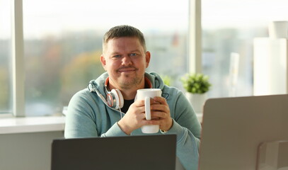 Handsome smiling male student using online education service and drink tea or coffee. Young man...