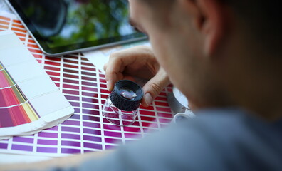 Male serviceman hold in hand magnifying glass making colour test at worktable for further promotion...