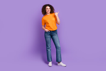 Full length photo of pretty sweet lady dressed orange t-shirt pointing thumb empty space isolated violet color background