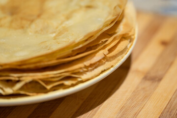 Thin pancakes on a white plate on the table, close up. Yellow crepes with crispy edge, just fried, ready to be eaten