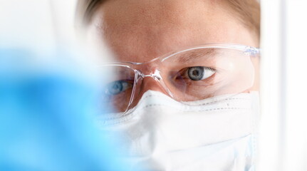 A portrait of a young surgeon chemist's doctor looks at a container with a blue liquid and a mask...