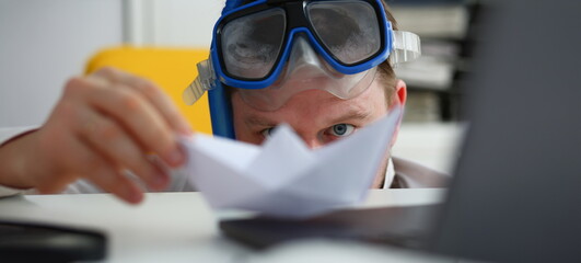 Man wearing suit and tie in goggles and snorkel play with paper ship in office portrait. Count days...