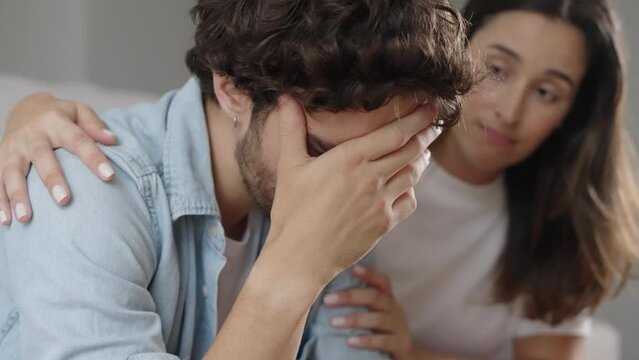 Young caucasian sad man sit on couch at home suffer worried breakdown regret erectile dysfunction loving woman wife hug comforting support empathy crisis impotence potency health
