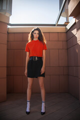 a beautiful modern girl in a red sweater and a black skirt poses in an industrial location. Fashion magazine