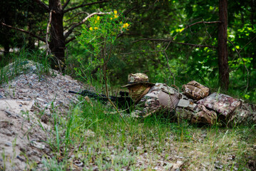 A soldier in camouflage lies in the green grass