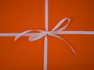 A white bow on an orange paper background. - obrazy, fototapety, plakaty