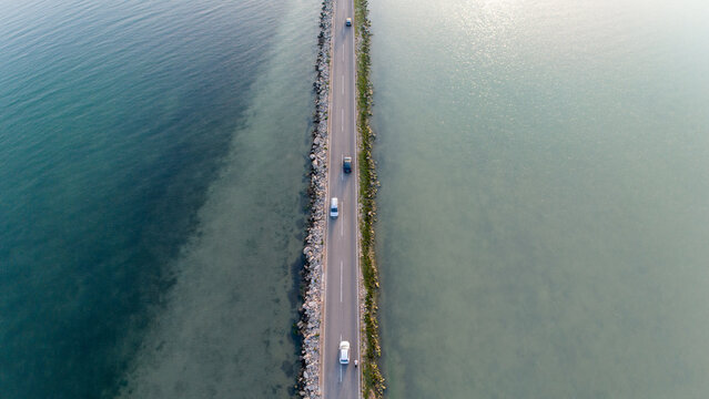 Aerial photo of the traffic on a road across a bay surrounded by blue and  green sea.