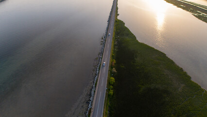 Aerial photo of two cars driving on a road across a bay in the light of setting sun.